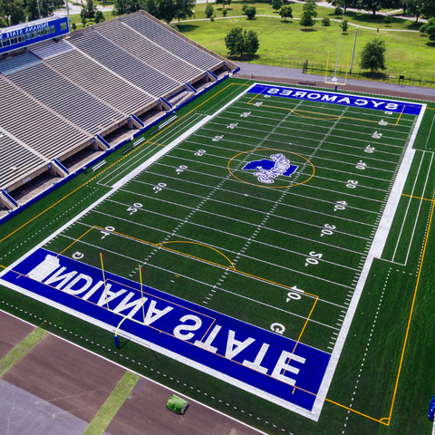 Aerial view of the Indiana State University football field with 'Sycamores' and 'Indiana State' painted on the turf. The stadium seating is visible in the background.